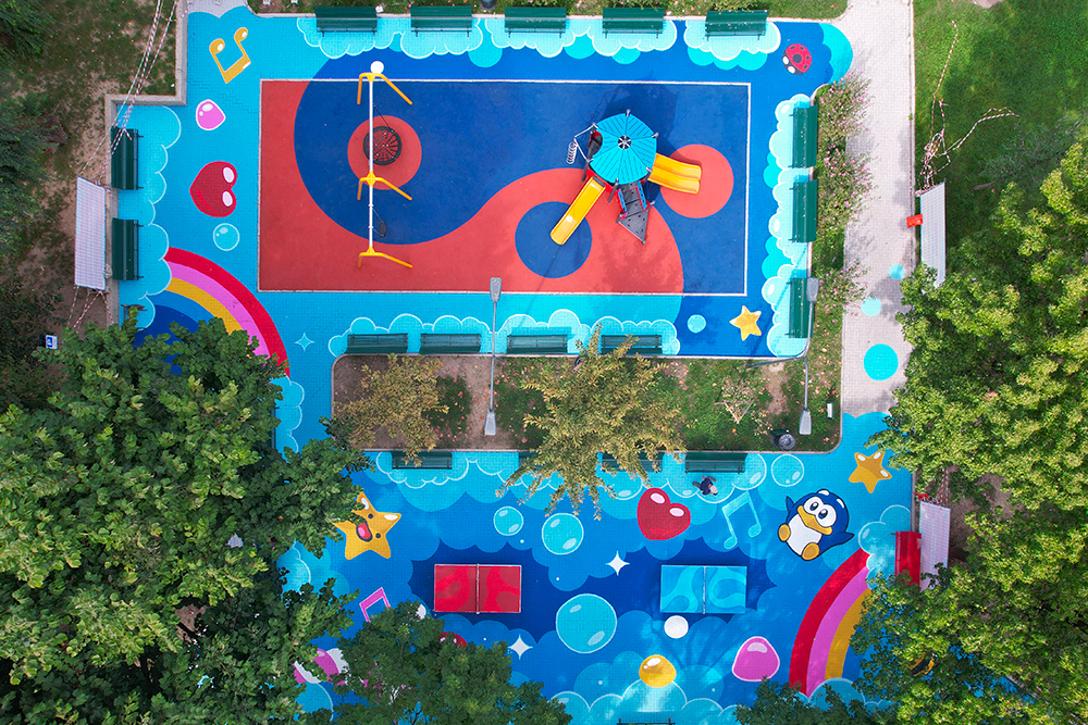 Vista aerea di Piazza Belloveso a Milano dopo l’intervento di PAO per HARIBO: un playground trasformato in Happyland con floor painting colorato tra arcobaleni, bolle, stelle e il pinguino PEO gigante