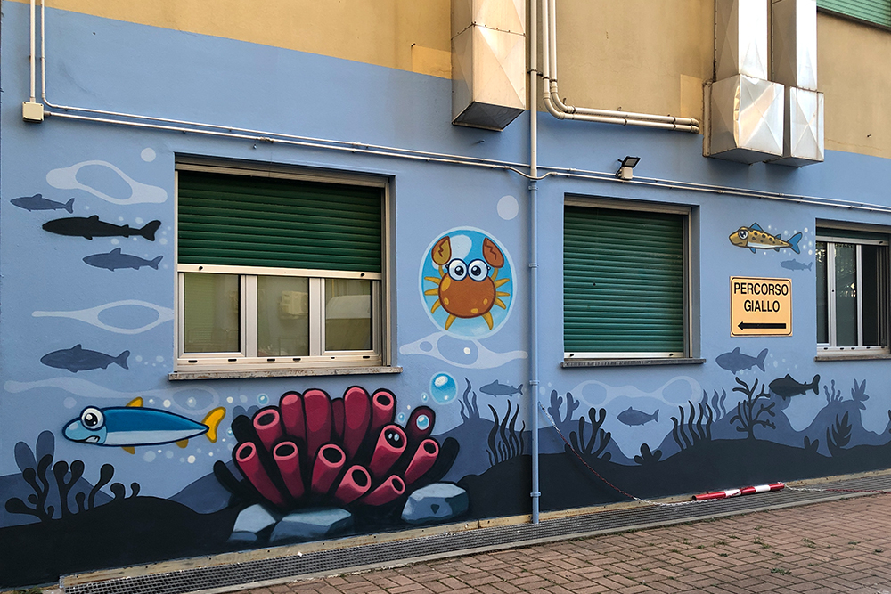 pesci sardine e granchi disegnati da pao sul muro del nuovo atrio dell'ospedale gaslini di genova nel 2025